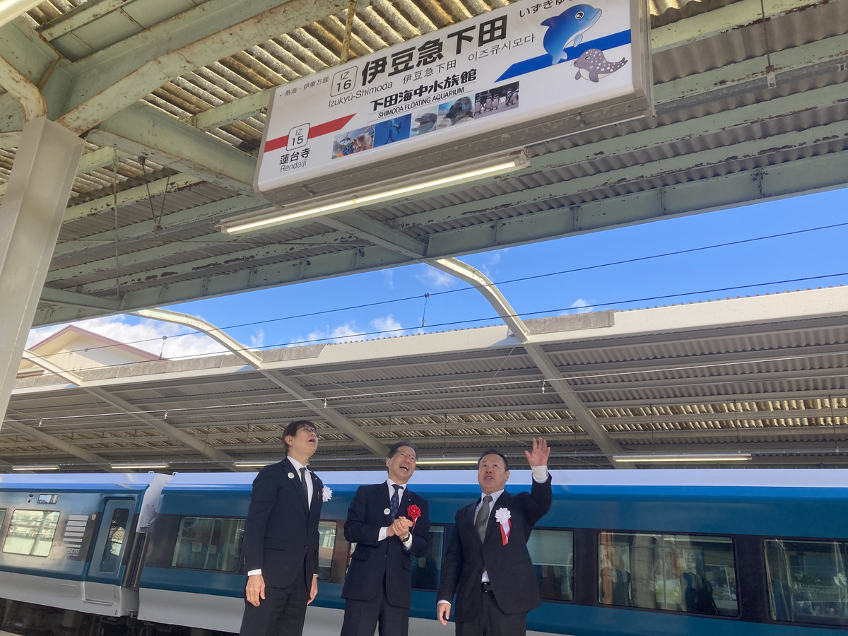伊豆急下田駅の駅名看板を見上げる伊豆急行の土方健司社長（中央）たち